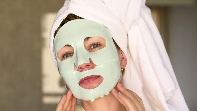 Woman with towel on head adjusting hydrating cryo rubber face mask, showing skincare routine, soft natural light and clean beauty mood. Perfect for wellness content, spa themes, cosmetic ads, selfcare