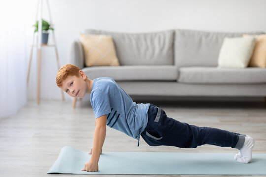 An athletic redhead boy in sportswear is planking on a fitness mat at home. He is focused while exercising in the living room, promoting a healthy lifestyle for kids.