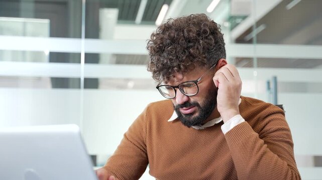 Unhealthy businessman suffers from ear pain sitting at workplace in business office. The man touches his ear with fingers. Worker has furuncle, shingles, eczema, ear diseases or otitis media. Close up