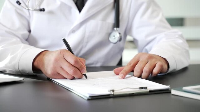 Close up of doctor's hand signing medical documents in hospital office. Physician in lab coat reviewing a report on clipboard, writing prescription, filling out patient records or treatment conclusion