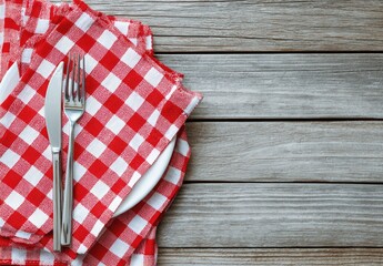 Red checkered cloth napkins, white plate, fork, knife on a wood table