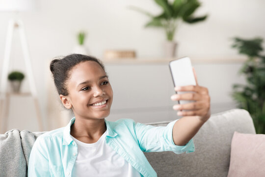 Cheerful teen girl records a video for social media in her living room during covid-19 quarantine. She is capturing moments while staying connected with friends and followers. - Powered by Adobe