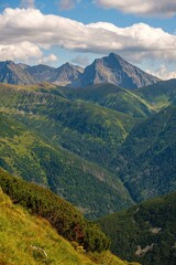 Snowy mountain peak glows in warm sunrise light above a quiet winter landscape. A small wooden cabin and bare trees stand in a pristine snowfield under dramatic morning clouds.Krivan peak High Tatras