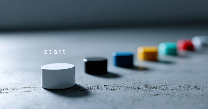 Close-up of colorful game pieces lined up on textured surface with white piece in focus and word start indicating beginning or initiation