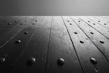 A low-angle view of dark, weathered wooden planks, studded with metal, receding into a stark grey background, highlighting texture and depth.