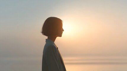 A woman s profile silhouette is illuminated by the warm glow of a hazy sunset over a calm sea evoking feelings of serenity contemplation and peaceful solitude at dawn or dusk