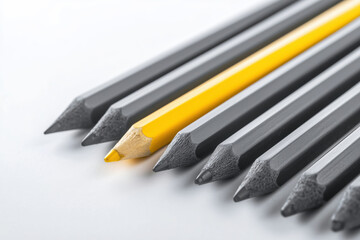 A sharp, yellow pencil stands out among several identical gray pencils lying diagonally on a white surface. High contrast. Individuality, leadership, uniqueness concept.