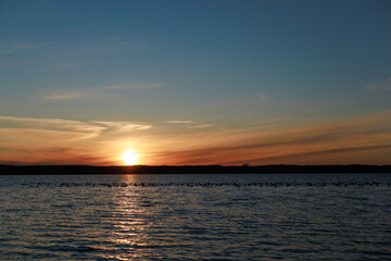 Sunset over calm lake. Smooth lake surface under colorful sunset sky. Concept of peaceful evening atmosphere, background use, nature design, and relaxation visual.