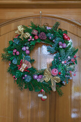 Christmas wreath on wooden door. Decorated Christmas wreath hangs on a wooden door with warm festive tones. Concept of holiday design, retail advertising, seasonal marketing, and greeting visuals.