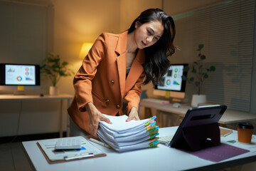 Asian businesswoman managing paperwork late working in office