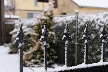 Metal fence with snow detail. Decorative metal fence covered with snow in a suburban garden. Concept of winter structure texture, architecture detail, and outdoor background.