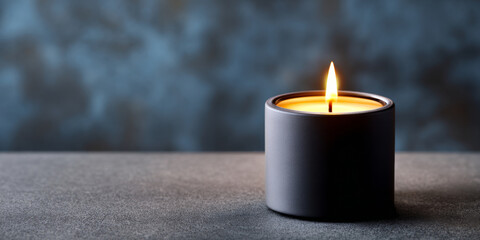 Single lit candle in a dark ceramic holder on textured surface with blurred blue background creating warm ambient light
