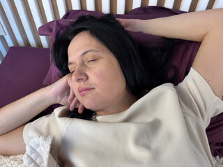 Adult brunette woman peacefully sleeping in bed in natural pose, cozy bedroom morning atmosphere, healthy sleep concept, relaxation, deep rest and stress relief