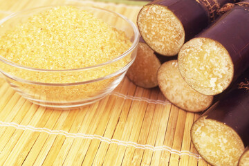 Brown sugar in wooden bowl and sugar cane sticks close up