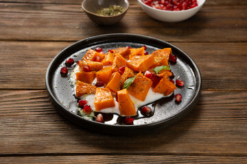 Close up of roasted pumpkin slice on black plate wooden surface