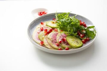Fresh salad with sliced watermelon radish on plate  light surface close up