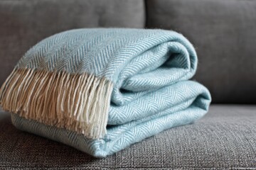 Folded light teal herringbone throw blanket on a gray sofa