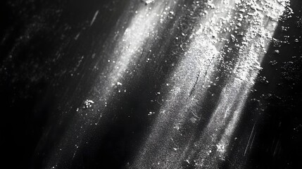 An abstract close up shows white powder dusted diagonally across a dark, textured surface with harsh lighting.