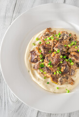 Braised meat and mushroom topping over creamy mashed potato served on white plate