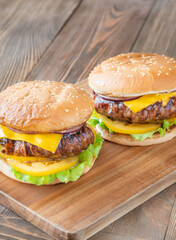 Two cheeseburgers with bacon and yellow tomato slices on rustic wooden board