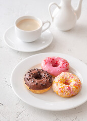 Trio of glazed donuts with coffee cup and pitcher in bright morning light