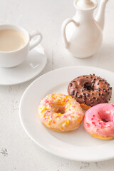 Trio of glazed donuts with coffee cup and pitcher in bright morning light