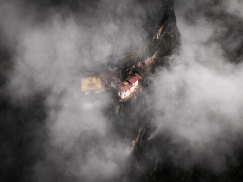 Aerial view of the iconic Tiger's Nest monastery clinging dramatically to the cliffside, shrouded in ethereal mist and clouds, Paro, Bhutan.