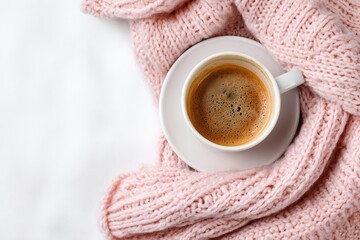 A cup of coffee on a white blanket, draped with a soft pink knitted throw