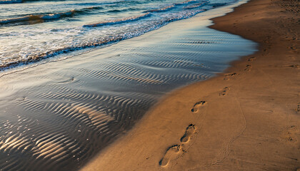 Footprints on a sandy beach with gentle waves and ripples.