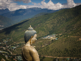 Aerial view of the serene Great Buddha Dordenma statue, gazing over the lush, green valley nestled beneath a backdrop of majestic, blue-tinged mountains, Thimphu, Bhutan.