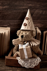 Vintage style teddy bear in paper ruff collar and a cap holding a gift box in sepia color