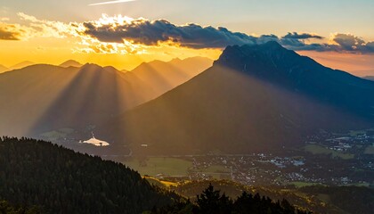 Sunlight streams over a valley with a lake and village, framed by green mountains at golden hour