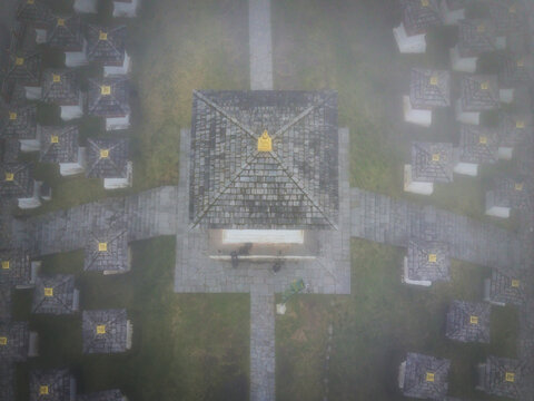 Aerial view of the Dochula Chorten shrouded in mist, its grey roofs contrasting with the vibrant prayer flags fluttering atop each small stupa, Hungtso, Bhutan.