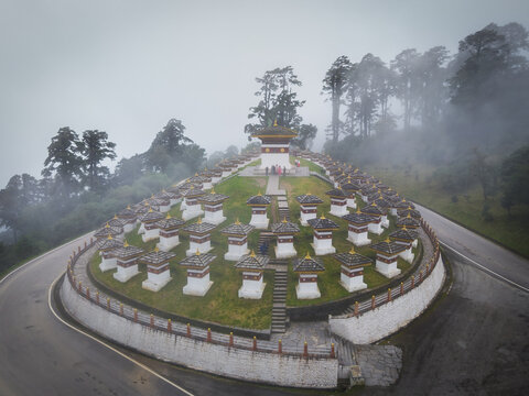 Aerial view of Dochula Chorten's 108 memorial stupas stand in orderly rows, painted white against the misty, mountainous backdrop, Hungtso, Bhutan.