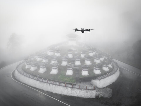 Aerial view of the Dochula Chorten shrouded in ethereal mist, with a drone hovering above the white stupas, Dochula pass, Hungtso, Bhutan.