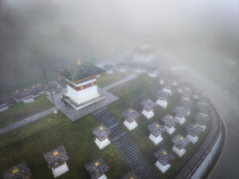 Aerial view of the Dochula Chorten's ethereal stupas pierce through the dense fog, their white facades and golden roofs creating a serene and mystical landscape, Hungtso, Bhutan.