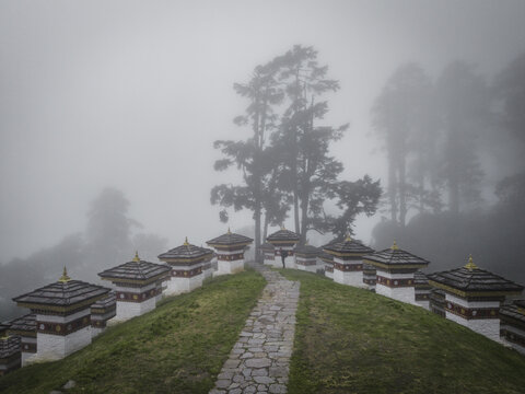 Aerial view of the Dochula Chorten's white stupas and a stone pathway cutting through the misty landscape, Dochula pass, Hungtso, Bhutan.