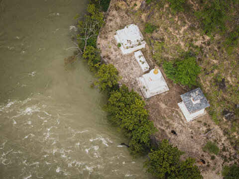 Aerial view of white stupas and prayer structures nestle beside the muddy confluence of rivers, contrasting with the vibrant greenery, Tenchhekha, Bhutan.