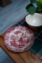 Elegant table setting with a detailed red plate featuring traditional architecture pattern, placed beside a white bowl on a checkered tablecloth for festive dining