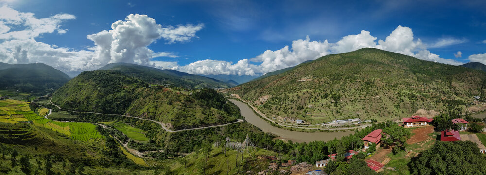 Aerial panorama view of a winding river cutting through lush green valleys beneath a sky alive with billowing clouds, Teoprongchu, Punakha, Bhutan.