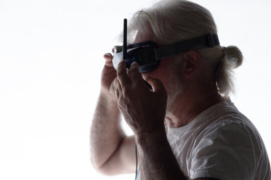 head profile of bearded elderly man operating FPV drone in googles on his head, studio shot of man and modern technologies