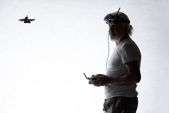 Silhouetted elderly man operating racing drone in goggles and remote control on studio background, modern hobby and technology