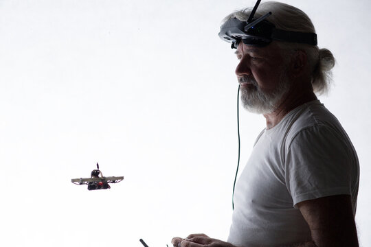 Silhouetted elderly man operating racing drone in goggles and remote control on studio background, modern hobby and technology