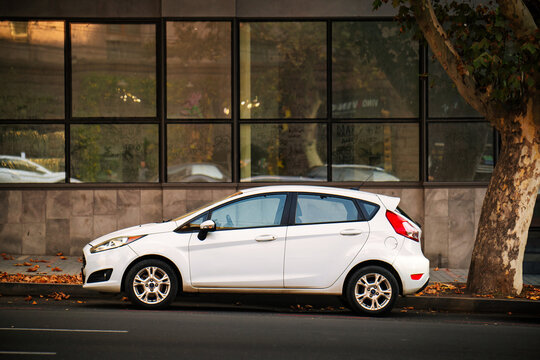 A white Ford car is parked on the side of the road in front of a building