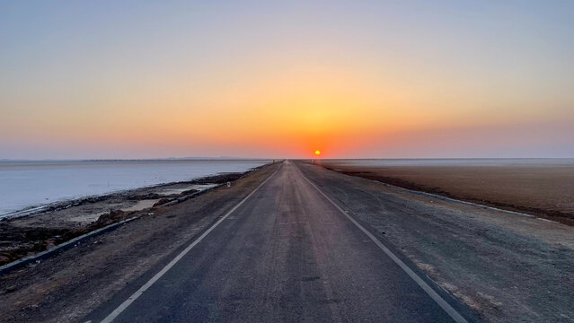 Endless road cutting through the white desert of Rann of Kutch, glowing under a surreal sunrise&mdash;capturing the feeling of driving straight into the horizon.