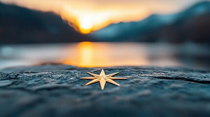 A golden star-shaped compass rests on a textured rock surface. In the background, a serene lake reflects the warm hues of a sunset, with blurred mountains silho