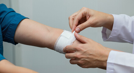 Nurse applying bandage on patient's arm in medical clinic setting  