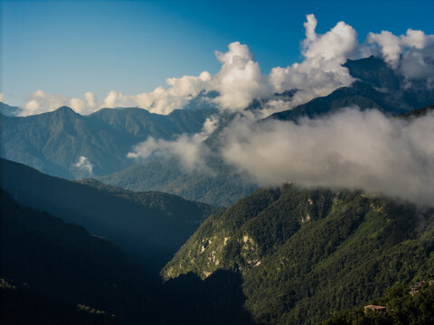 Aerial view of a dramatic landscape where the sun filters through the peaks, illuminating verdant slopes veiled in ethereal mists, Trongsa, Trongsa, Bhutan.