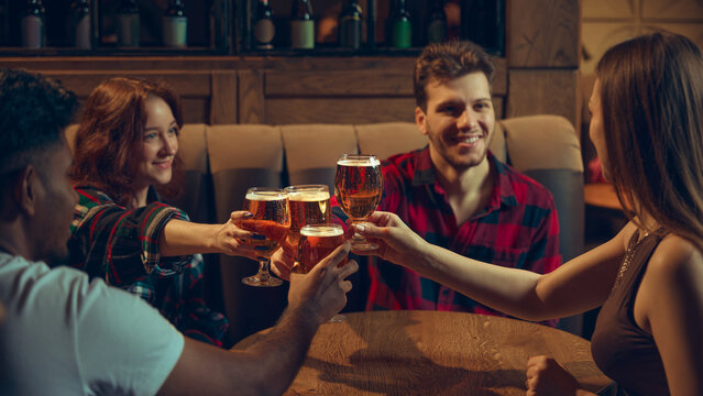 Friends clinking beer glasses in relaxed tavern setting. Concept of beer brand marketing, social nightlife scenes, casual bar community, festive events, and friendly leisure gatherings.