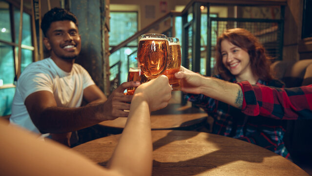Happy friends cheering beer mugs inside modern bar space. Concept of nightlife branding, club advertising, brewery outreach, weekend celebration visuals, and joyful social interactions.